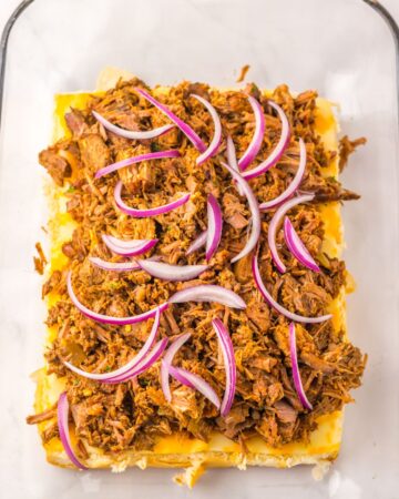 A large pyrex with slider buns topped with birria meat and red onions. 