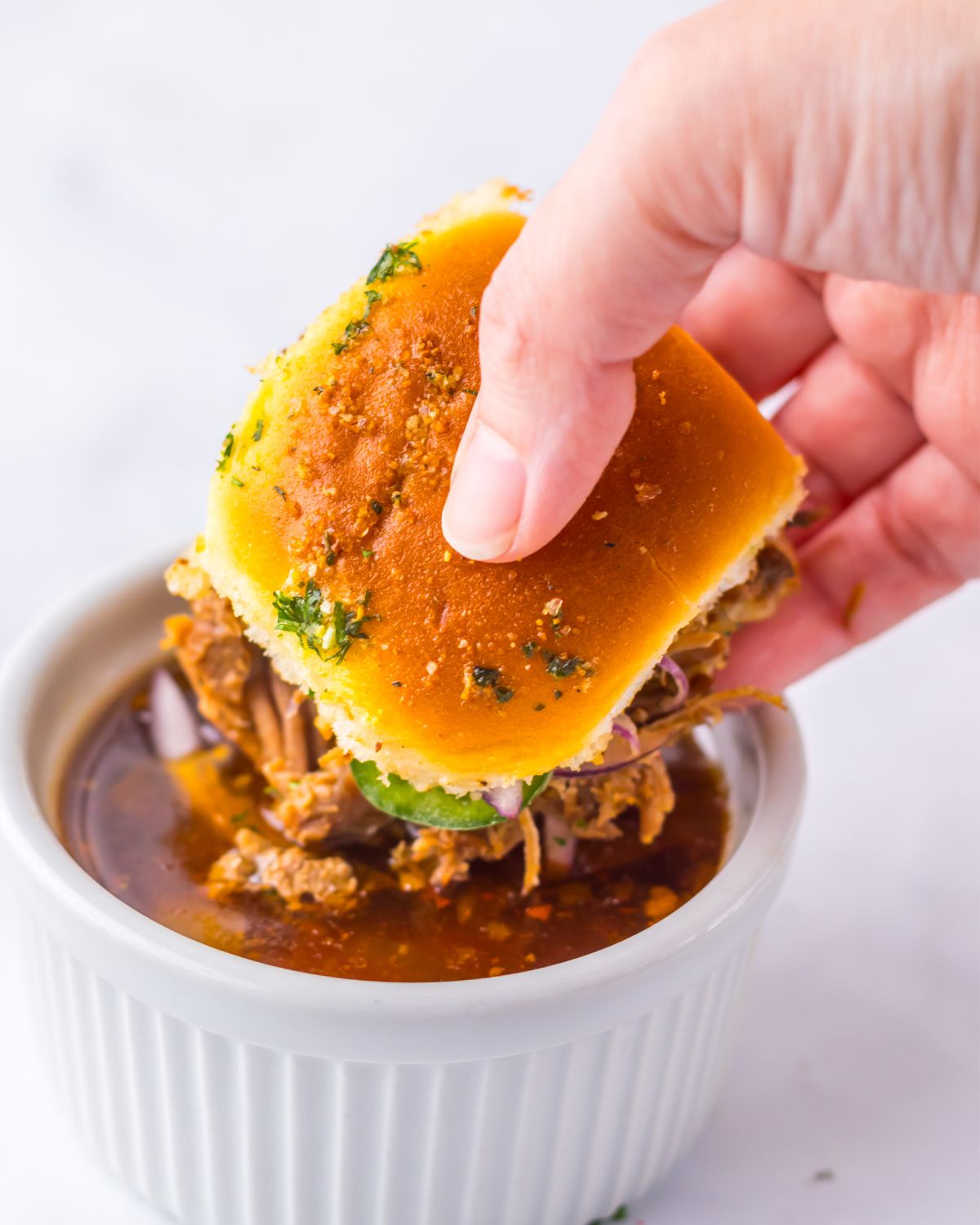 Slow cooked birria beef sliders being dipped into a sauce. 