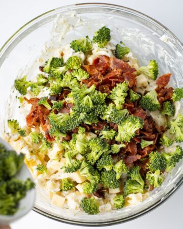 A glass bowl with tortellini, broccoli florets, and cheese to make a pasta salad. 