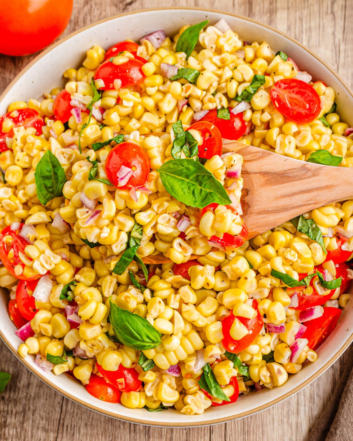 A bowl of corn salad with tomatoes, and basil.