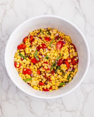 A bowl with the ingredients to make a corn tomato salad.