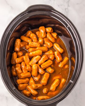 A slow cooker vessel with lil smokies ready to be cooked with Dr Pepper and BBQ Sauce.