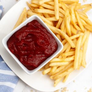 An overhead view of homemade ketchup in a bowl with french fries on the side.