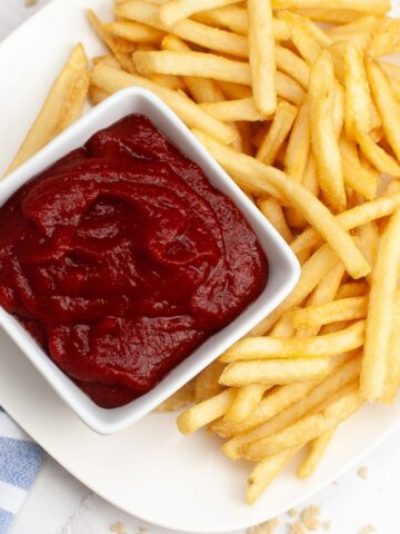 An overhead view of homemade ketchup in a bowl with french fries on the side.