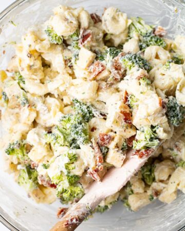 A glass bowl with cooked tortellini, bacon, broccoli, and cheese in a ranch dressing. 
