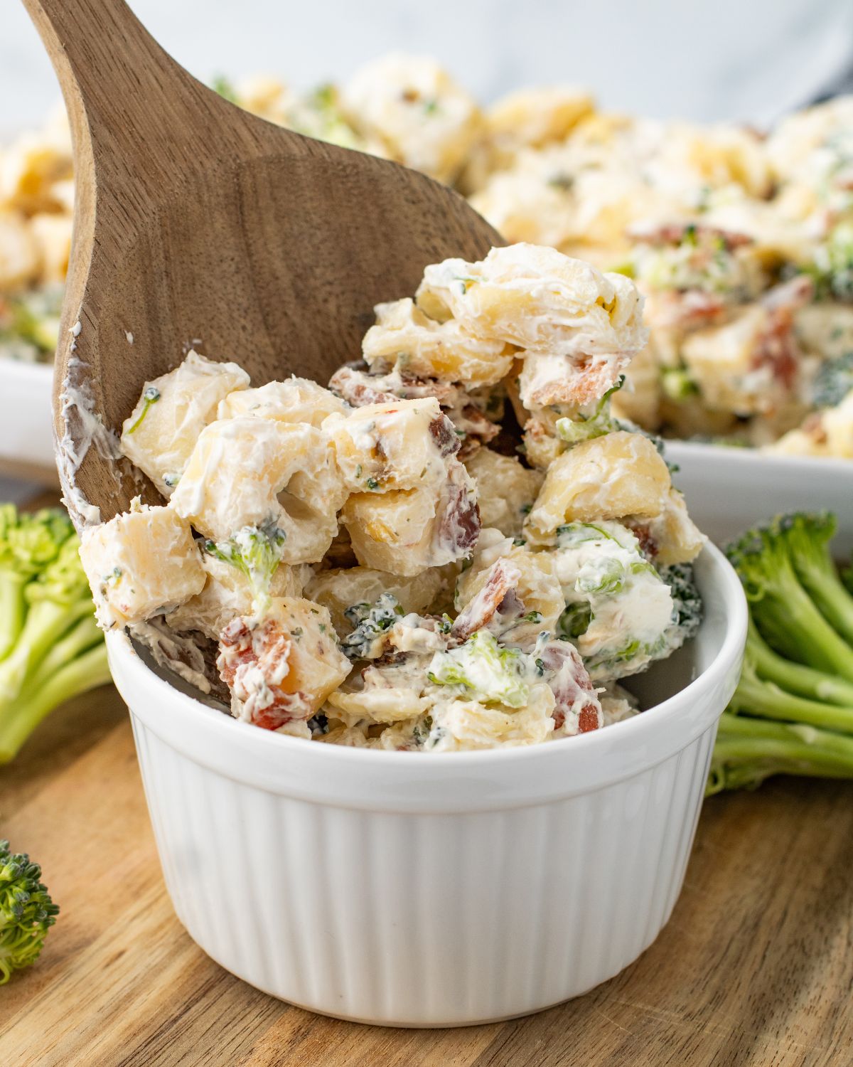 A white bowl with tortellini ranch salad in the bowl with a wooden spoon going into the bowl.