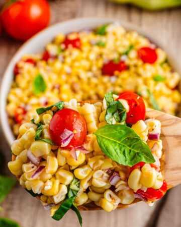 A tomato corn salad with basil on a wooden spoon.