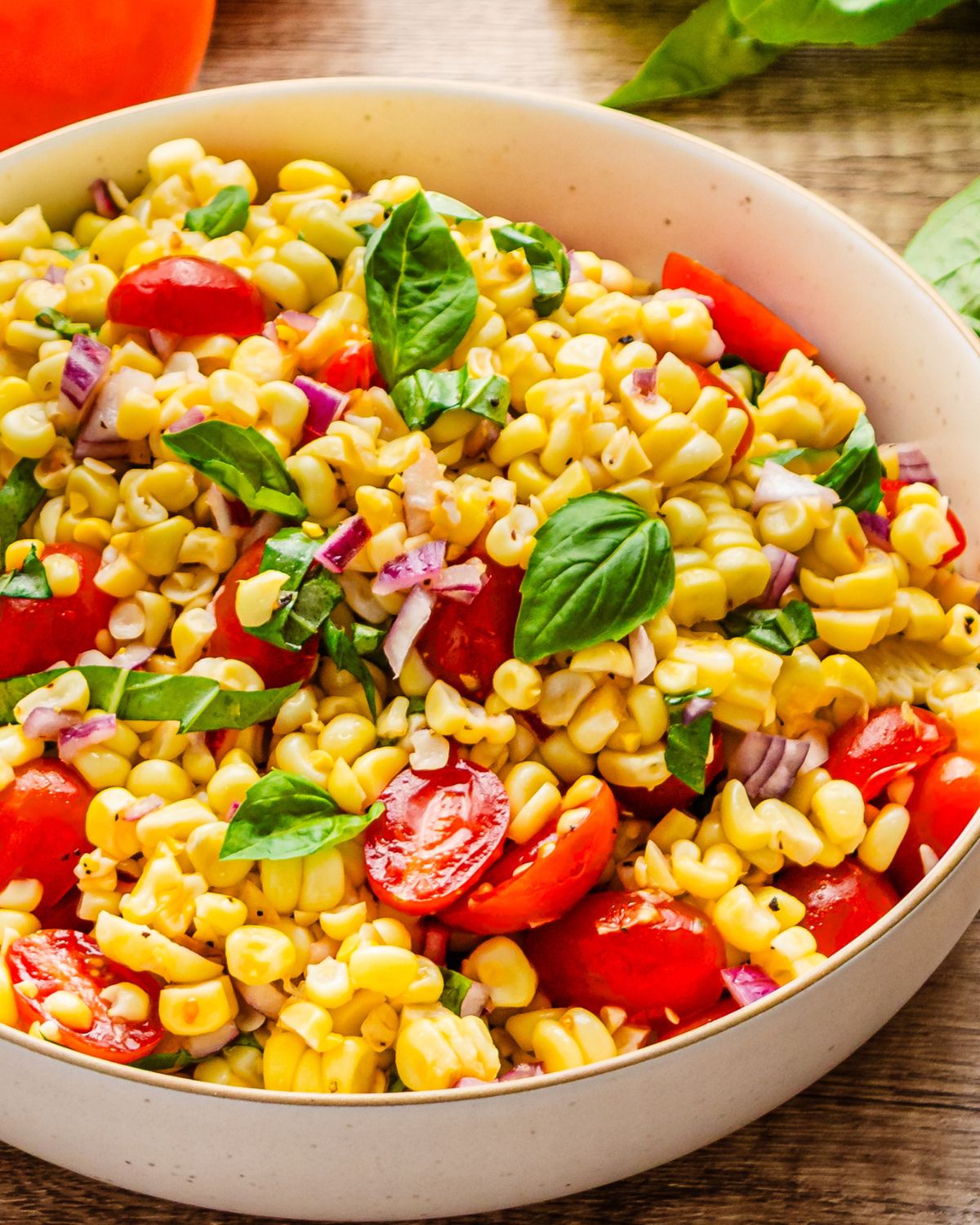 A side view of tomato corn salad with fresh basil in a bowl.