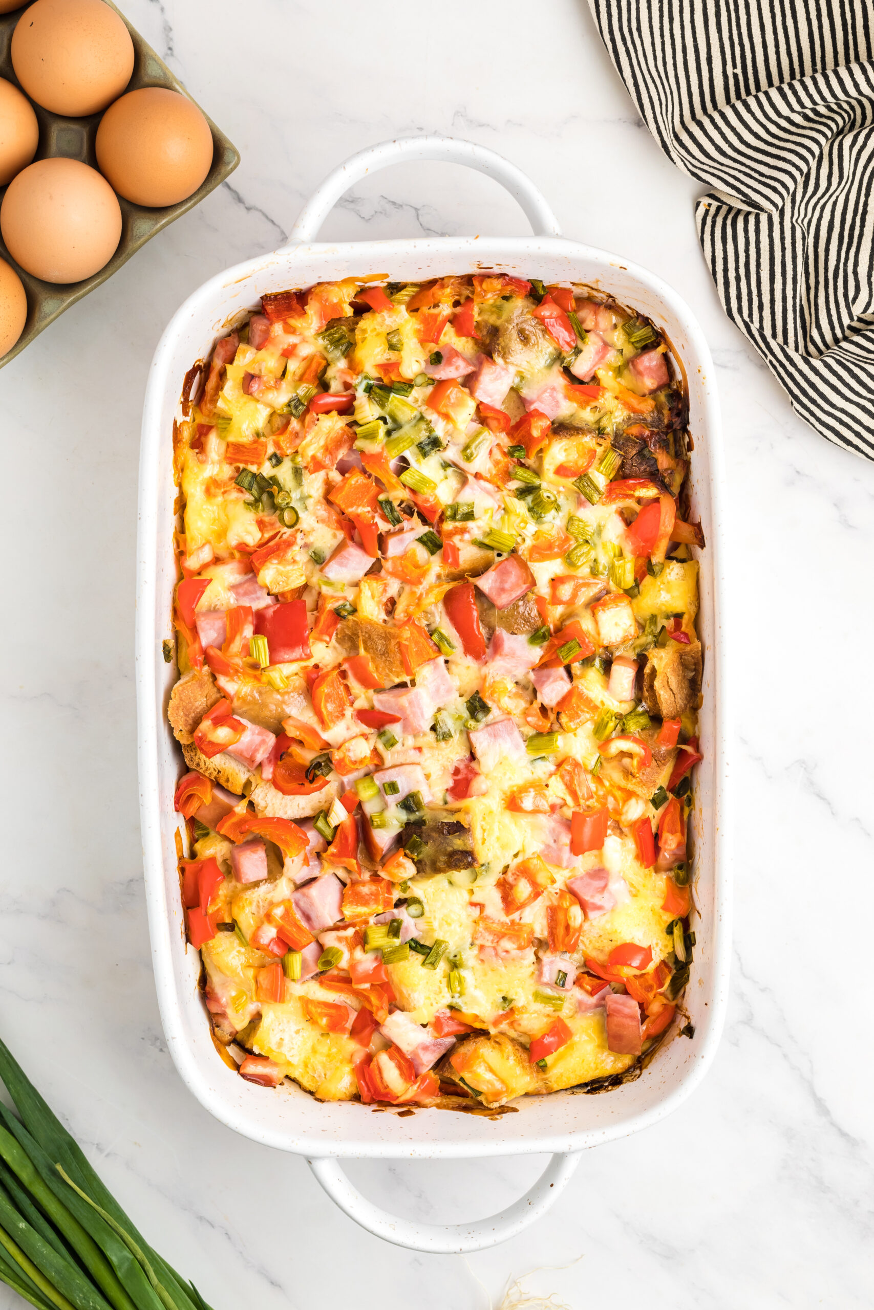 A white casserole dish with ham and eggs and bread.
