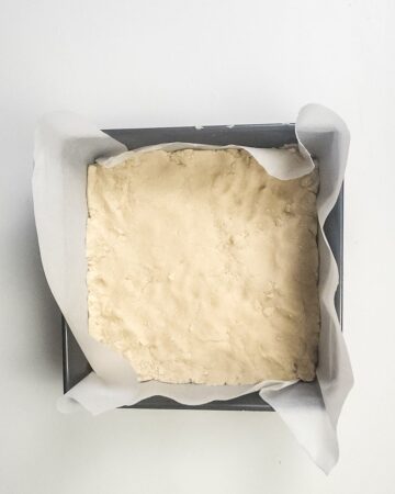 A square baking pan with a shortbread crust to be made into millionaire brownies.