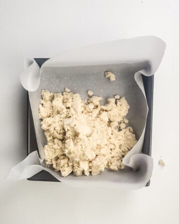 A square baking pan with the makings of a shortbread crust for millionaire brownies. 