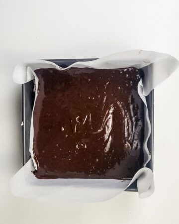 A square baking pan with parchment paper in the bottom that is in the process of forming millionaire brownies.