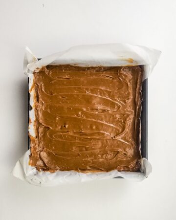 An 8 x 8 inch baking pan with the layer of dulche le leche on shortbread to make millionaire brownies.