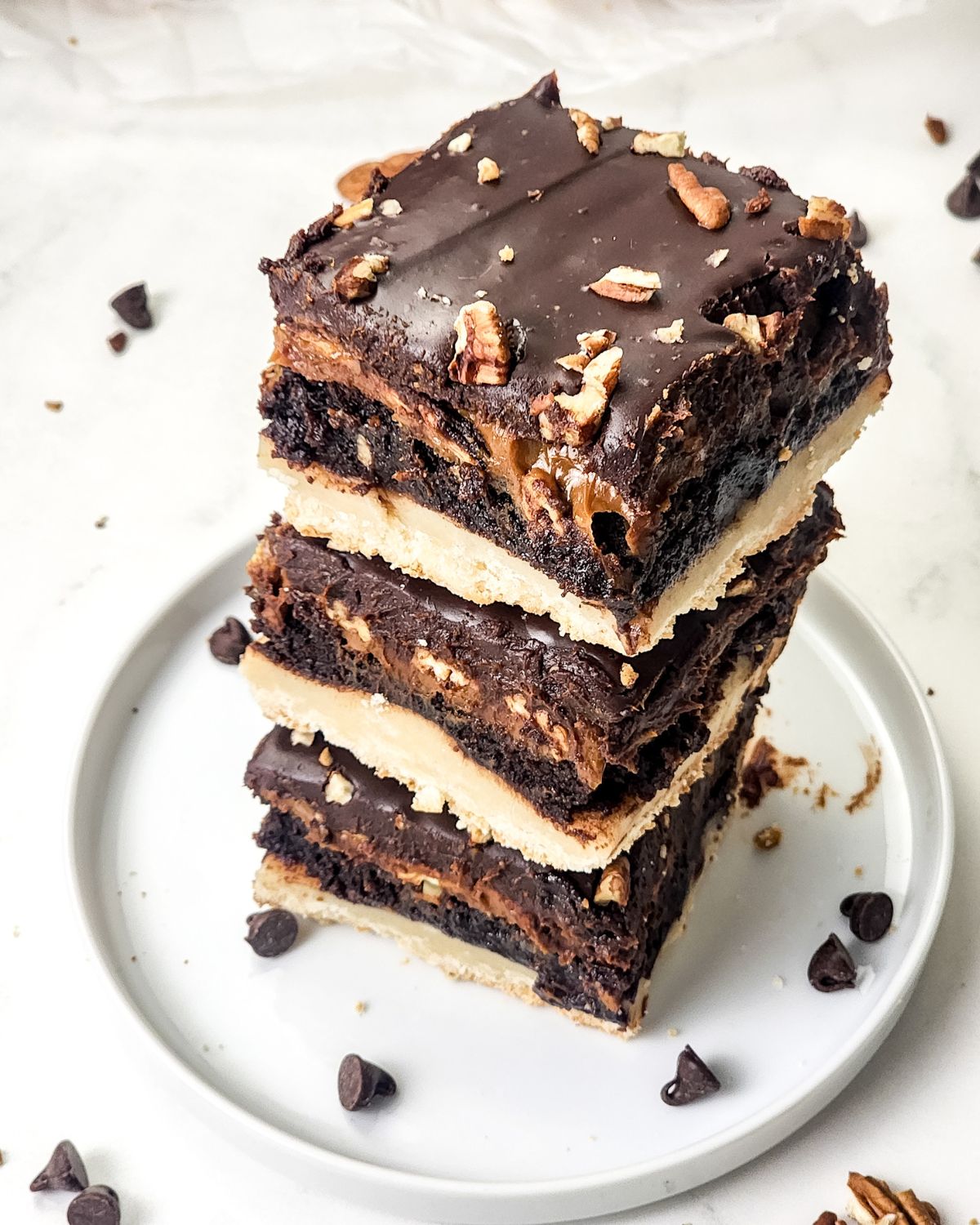 A stack of millionaire brownies on a white plate with chocolate morsels.
