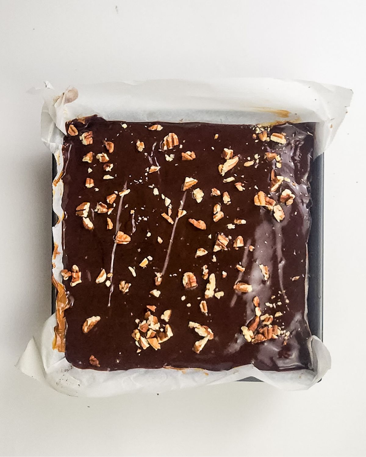 A square baking pan with millionaire brownies topped with a chocolate ganache and topped pecans.