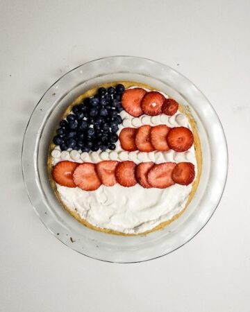 A glass pie dish with a sugar cookie base making a fruit flag pizza. Blueberries are the stars. Strawberries and marshmallows for the stripes.