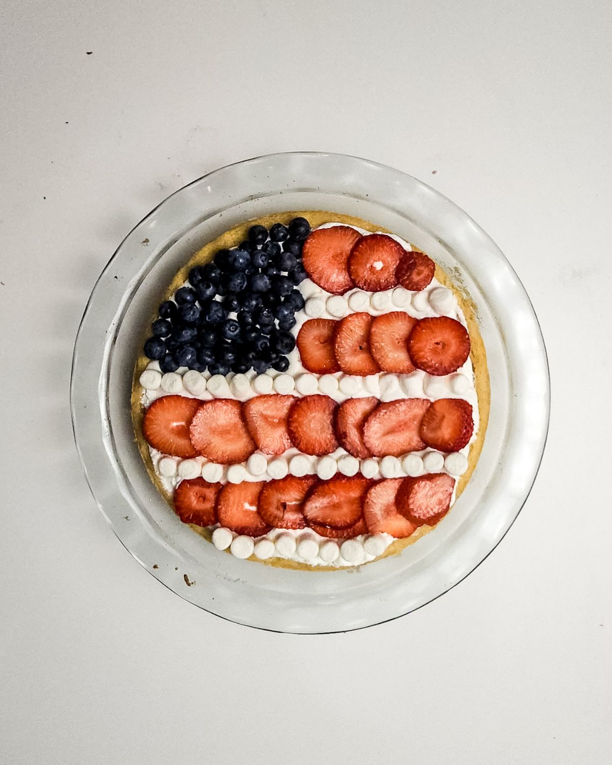A glass pie plate with a red white and blue fruit pizza shaped like the American flag.