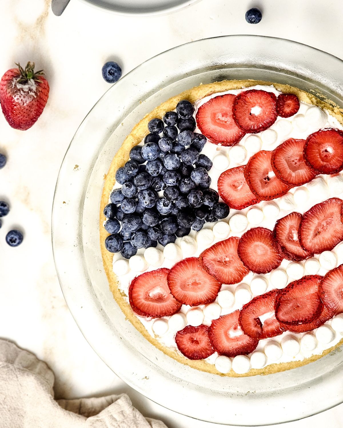 A glass pie plate with a sugar cookie red, white, and blue fruit flag pizza in the plate.