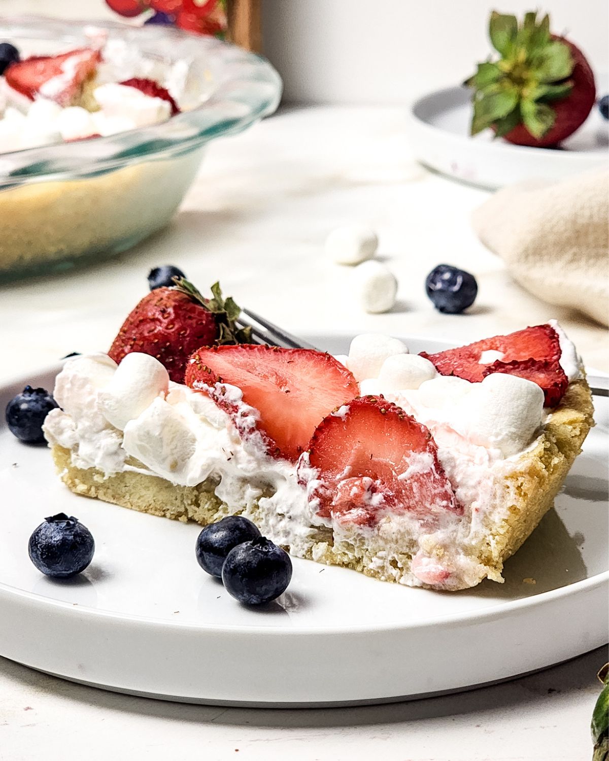 A white plate with a slice of sugar cookie fruit pizza that depicts an American flag.