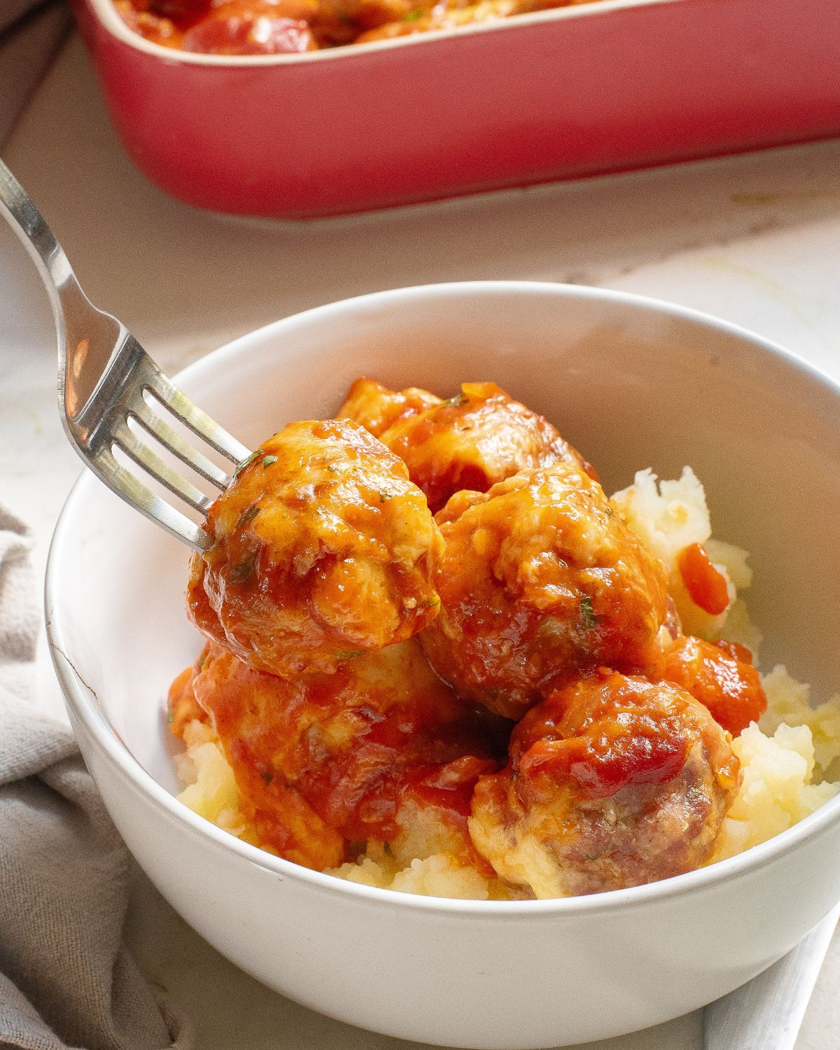 A white bowl of enchilada meatballs topped with melted jack cheese over meatballs.