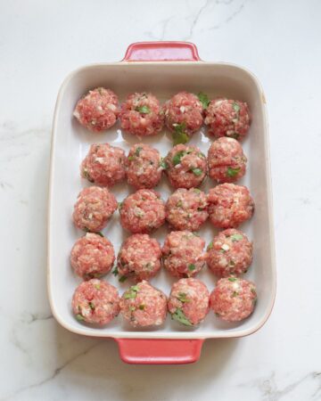 A casserole dish with unbaked enchilada meatballs in the dish.