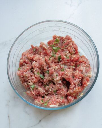 A glass bowl with ground beef, ground pork and other ingredients to make enchilada meatballs.