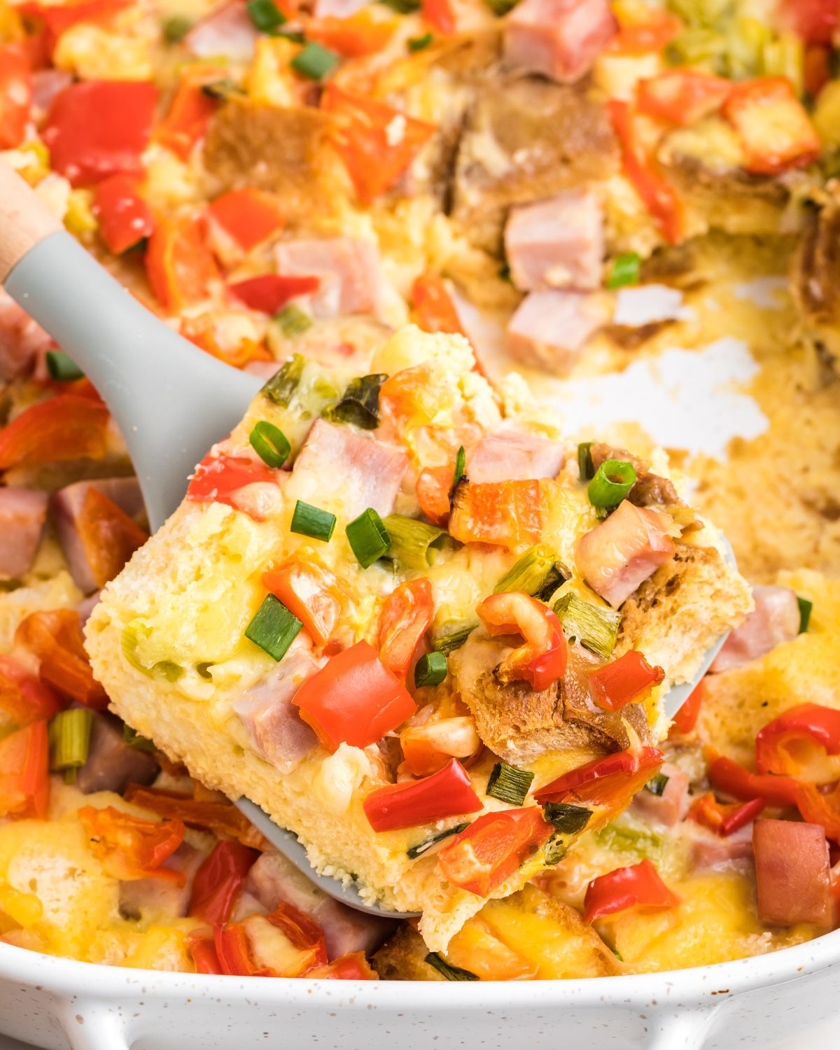 Ham and Egg Casserole with red peppers cut into squares and being picked up out of the casserole dish.