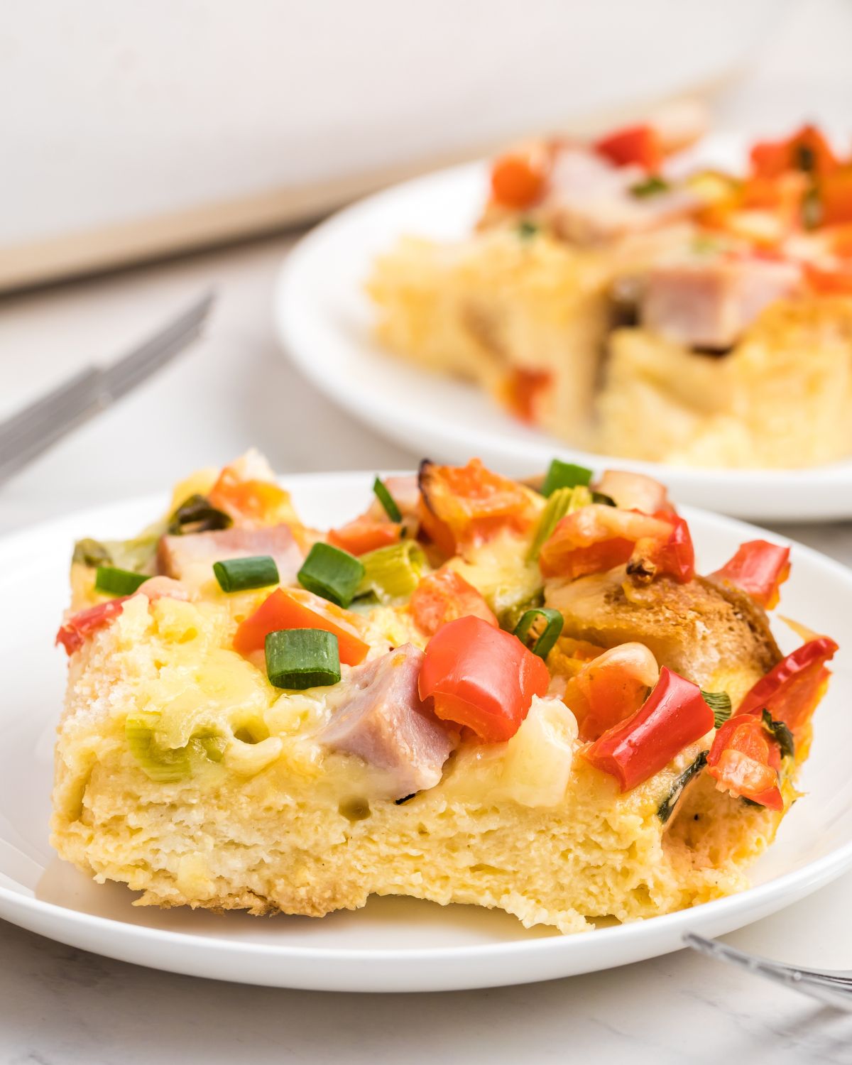 A white plate with a ham egg casserole topped with chopped green onions and diced red peppers.