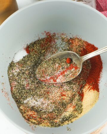 A bowl with homemade steak seasoning ingredients being mixed together with a spoon.