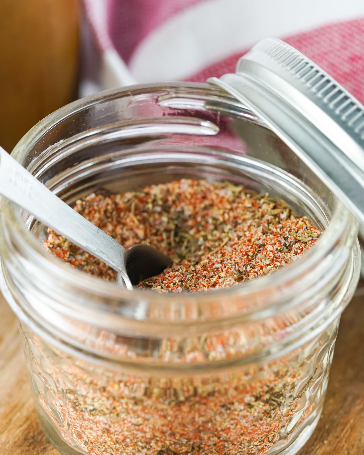 A glass mason jar with homemade steak seasoning and a measuring spoon in the jar.