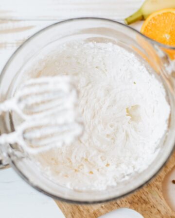 A glass mixing bowl with cream cheese and whipped topping in the bowl.