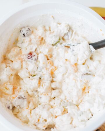 A white mixing bowl with whipped topping, cream cheese, fruit, and grapes to make a classic grape salad recipe.