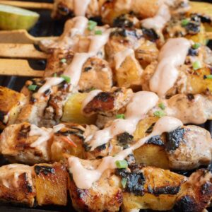 Bang Bang chicken skewers with bang bang sauce drizzled on the chicken and pineapple chunks.