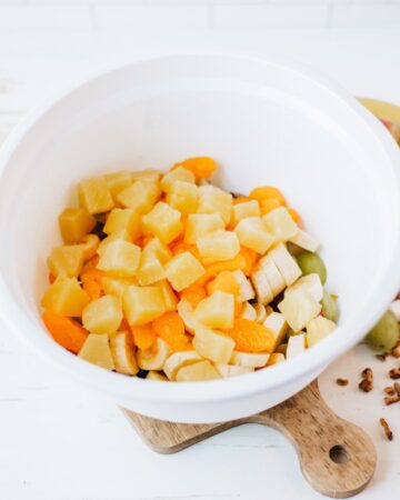 A white bowl with chopped fruit to make grape salad.
