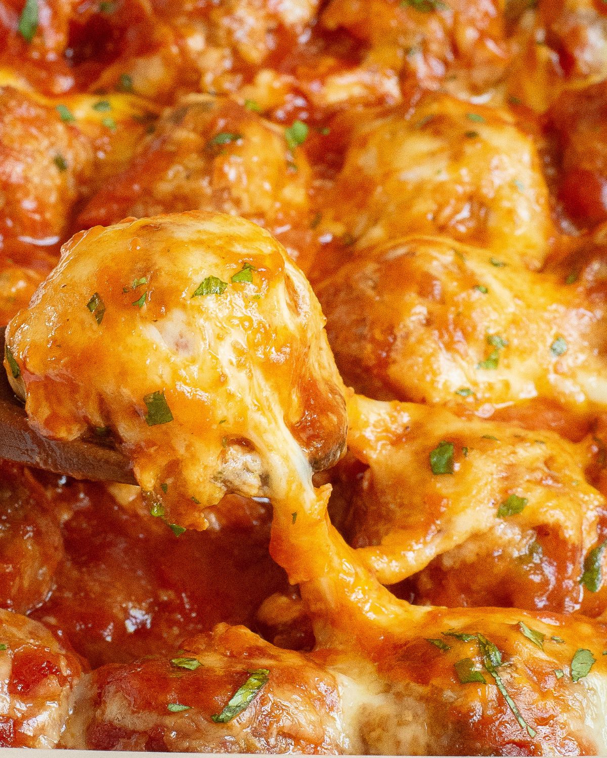 Meatballs in an enchilada sauce topped with cheese being picked up out of a baking dish.