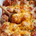 A baking dish with baked meatballs in enchilada sauce topped with melted cheese and sprinkled with chopped parsley.