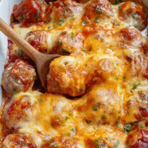 A baking dish with baked meatballs in enchilada sauce topped with melted cheese and sprinkled with chopped parsley.