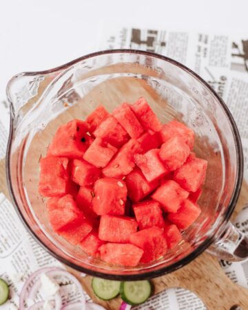 A glass measuring bowl with watermelon cubes in the cup.