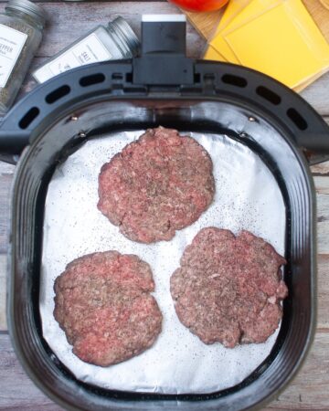 The vessel of an air fryer with 3 hamburger patties ready to be made in the air fryer.