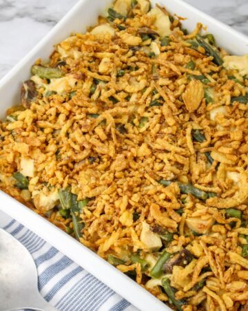 A white casserole dish with green beans and chicken in a mushroom sauce topped with fried onions ready to go into the oven.