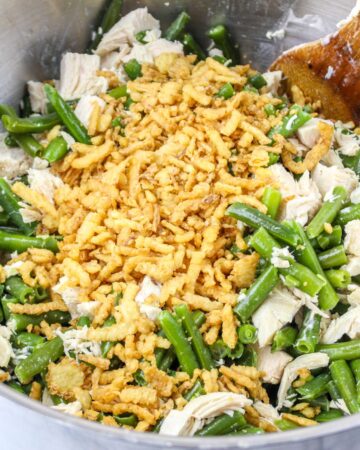 A mixing bowl with cubed chicken, green beans fried onions to make a green bean casserole with chicken.