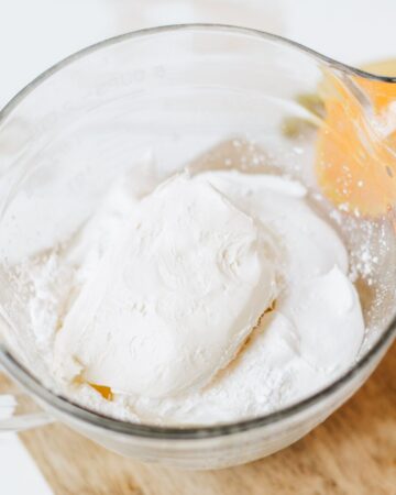A glass mixing bowl with cream cheese, confectioners sugar,