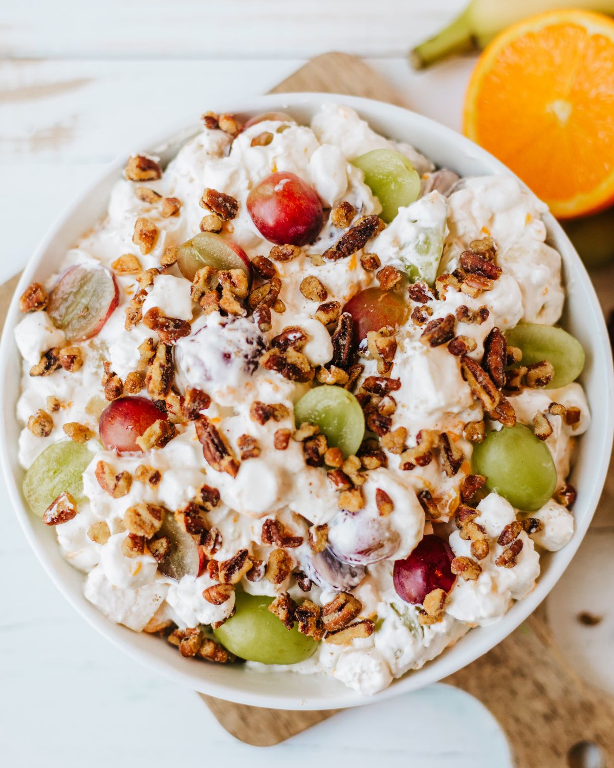 A white bowl with a classic grape salad with grapes, marshmallows and pecans.