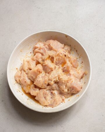 A white bowl with seasoned chicken pieces to make a sheet pan dinner.