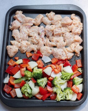 A sheetpan with cubed chicken and vegetables to make a chicken vegetable sheet pan dinner.