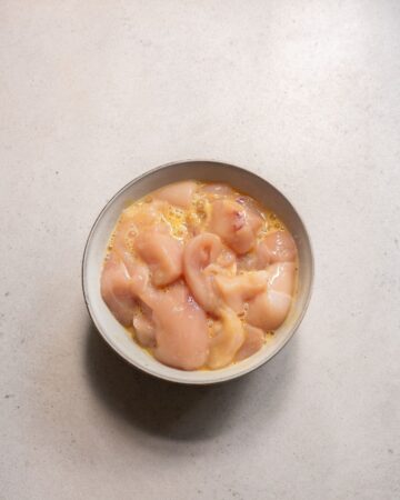 A white bowl with chicken in an egg base for a tasty sheet pan dinner.