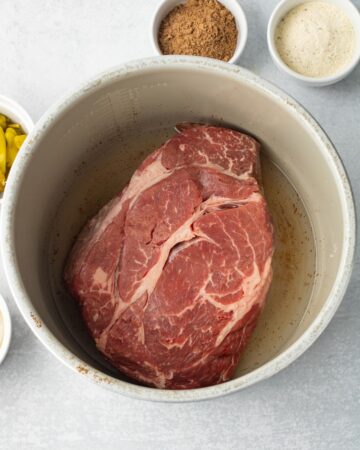 An instant pot with a chuck roast and water in the vessel.