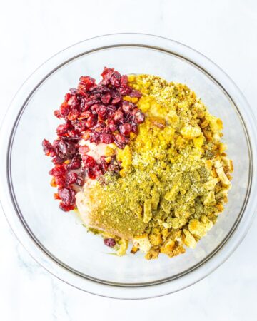 A glass bowl with dried cranberries, ground turkey, and stuffing mix.