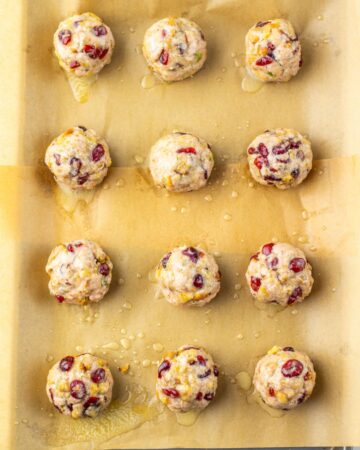 Uncooked turkey and dried cranberry balls on a baking sheet to make cranberry turkey stuffing balls.