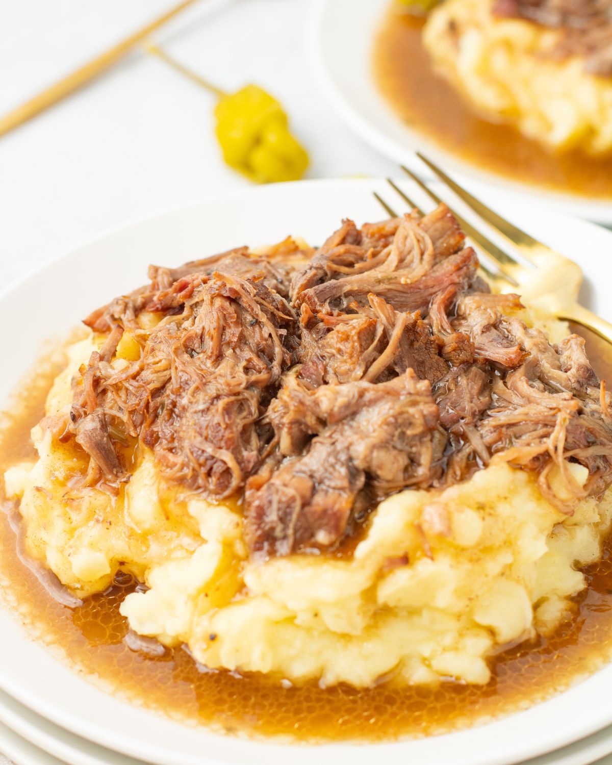 A plate with mashed potatoes topped with Mississippi pot roast and gravy.